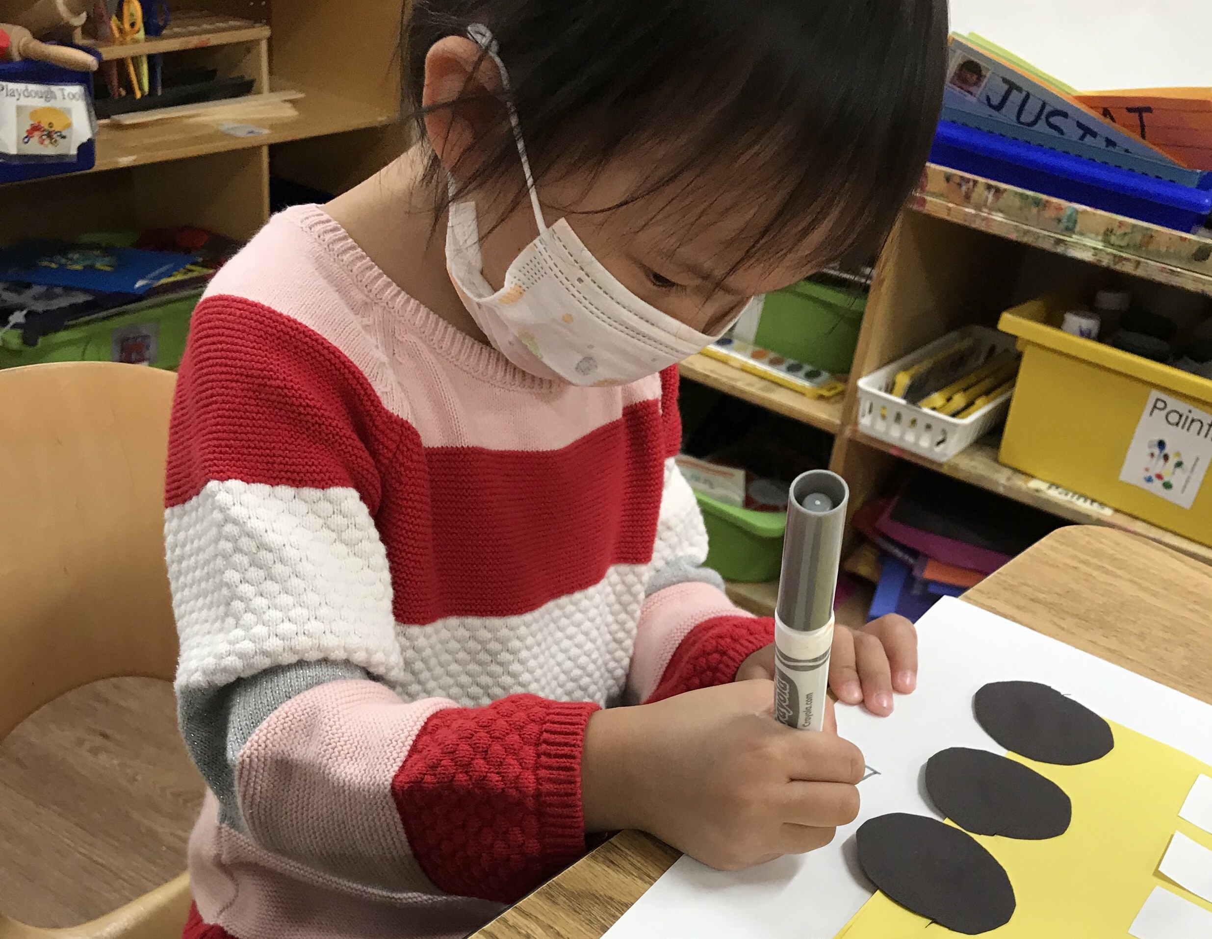 A child sitting at a table using a marker on a construction paper cut-out of a bus 