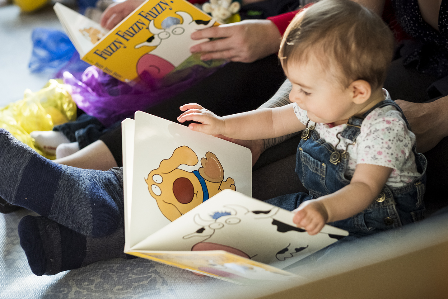 Baby sits on the floor with her parents and holds an open picture book
