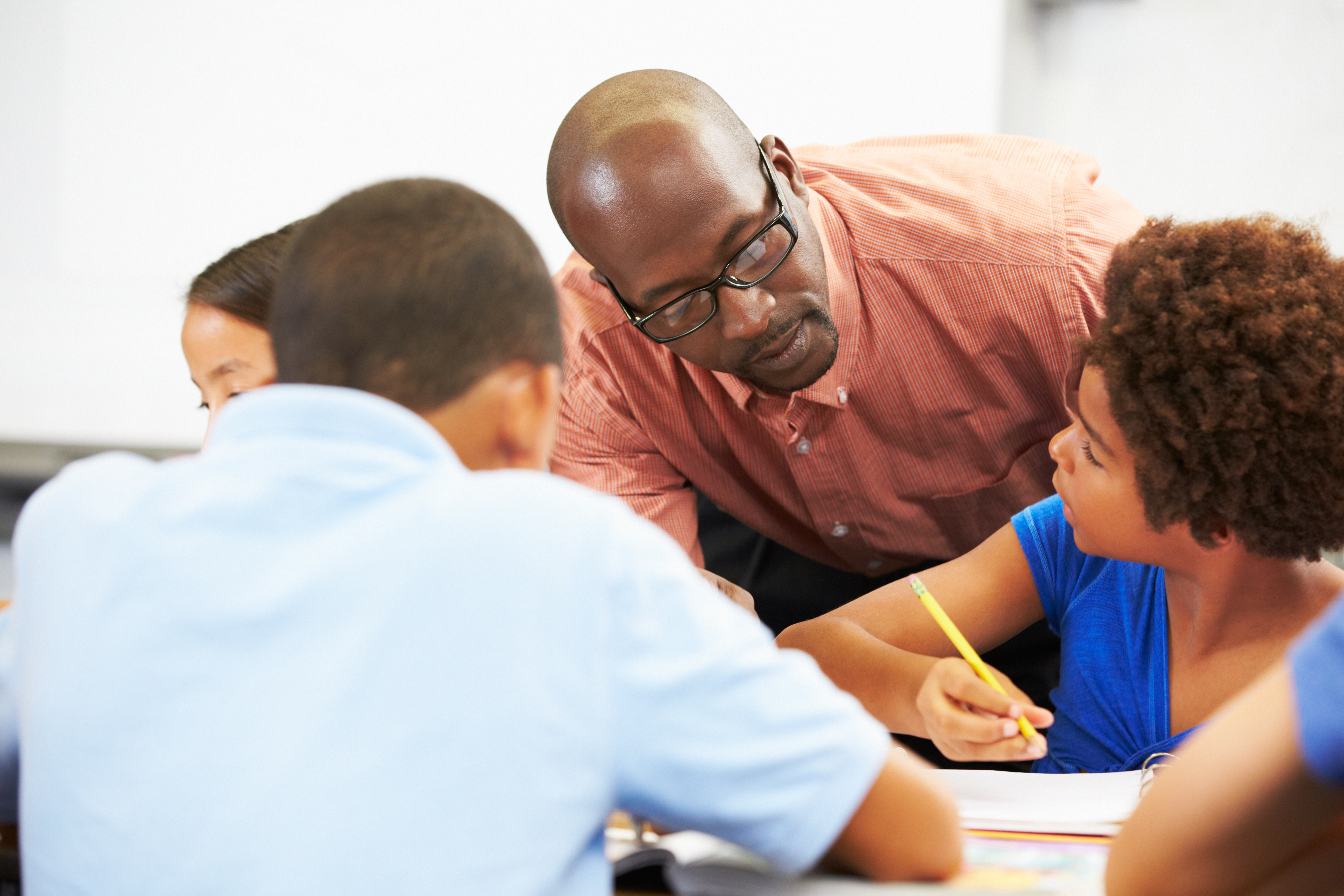 Teacher leaning over student with pencil in classroom