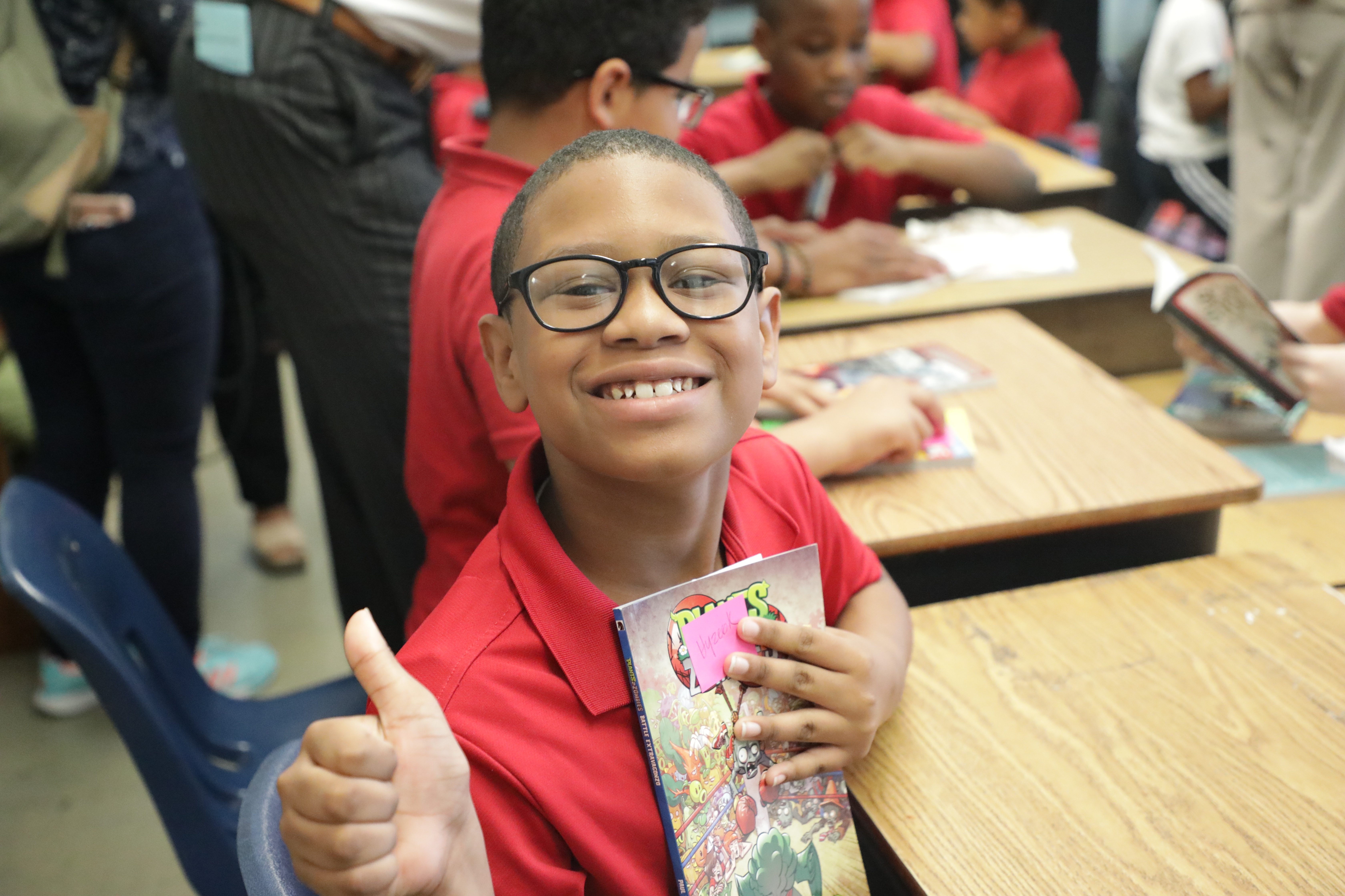 young child holding book to chest and giving thumbs up sign