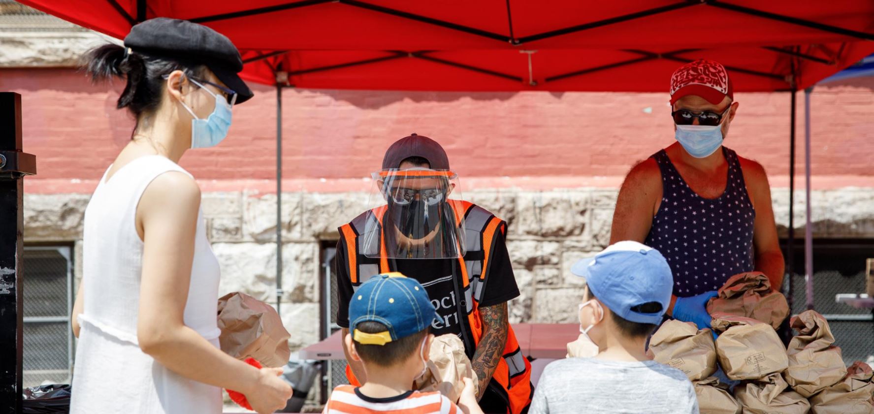 A mother and two children standing in front of a table where two people in face masks are distributing food.