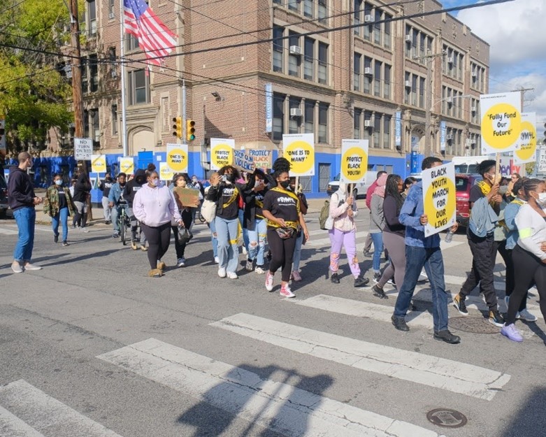A group of students marching in the street carrying signs with different slogans including "Black Youth March For Our Lives"