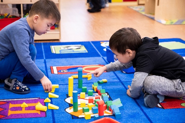 Two boys playing with blocks while sitting on a blue rug.