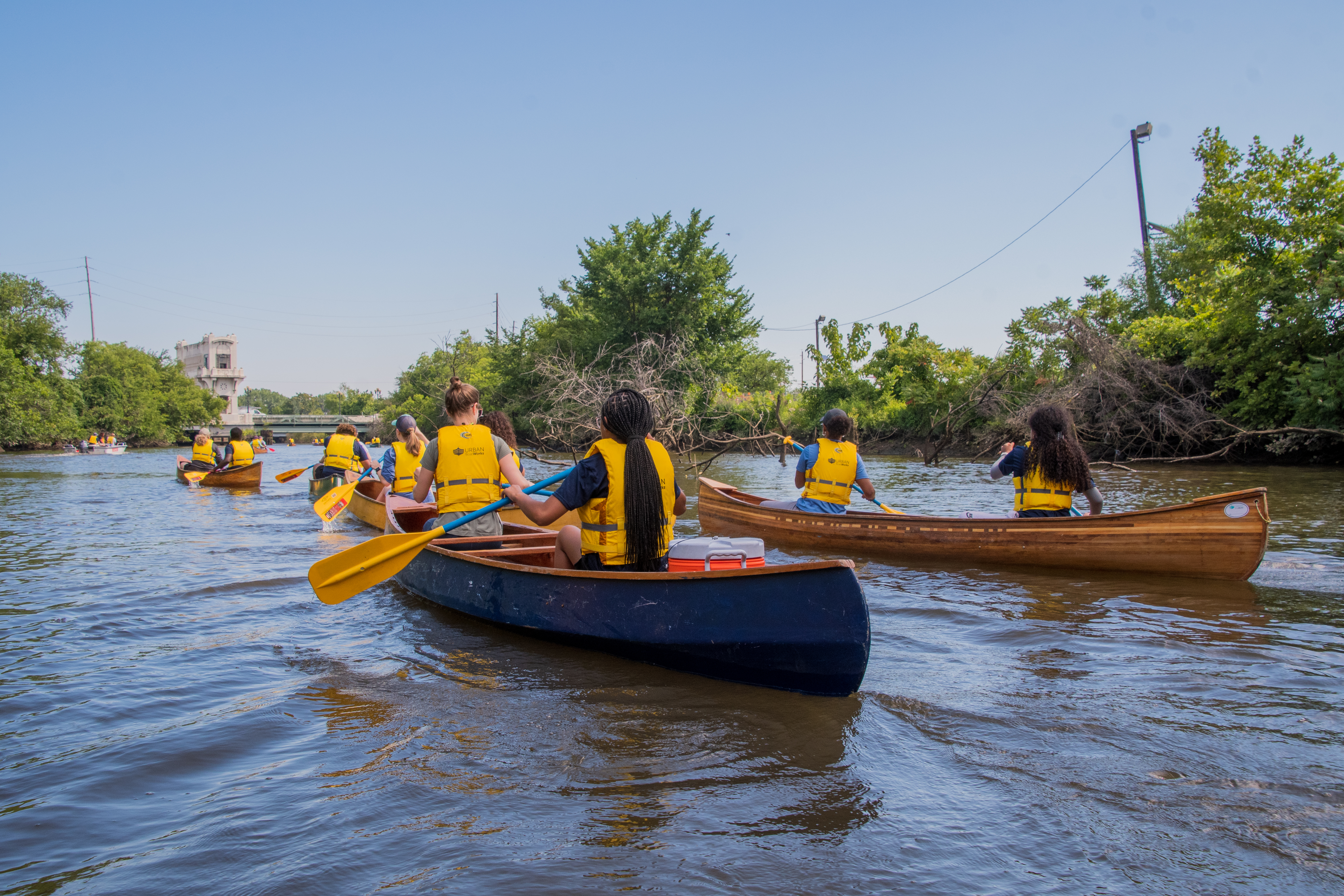 A group of people wearing yellow life vests, in canoes, on a river