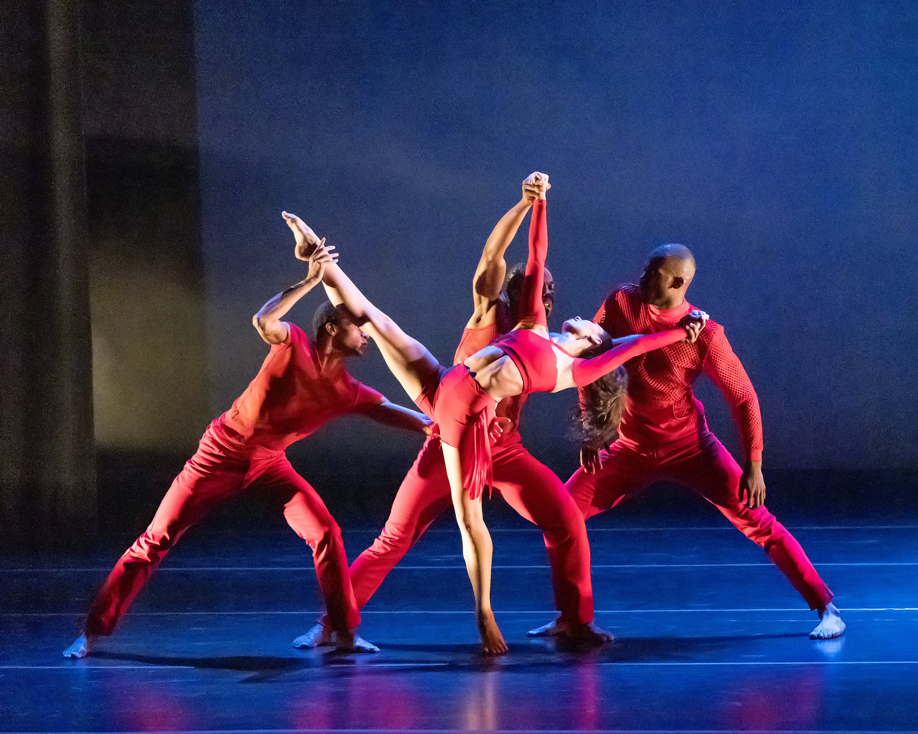 Four dancers dressed in red against a blue-lit background