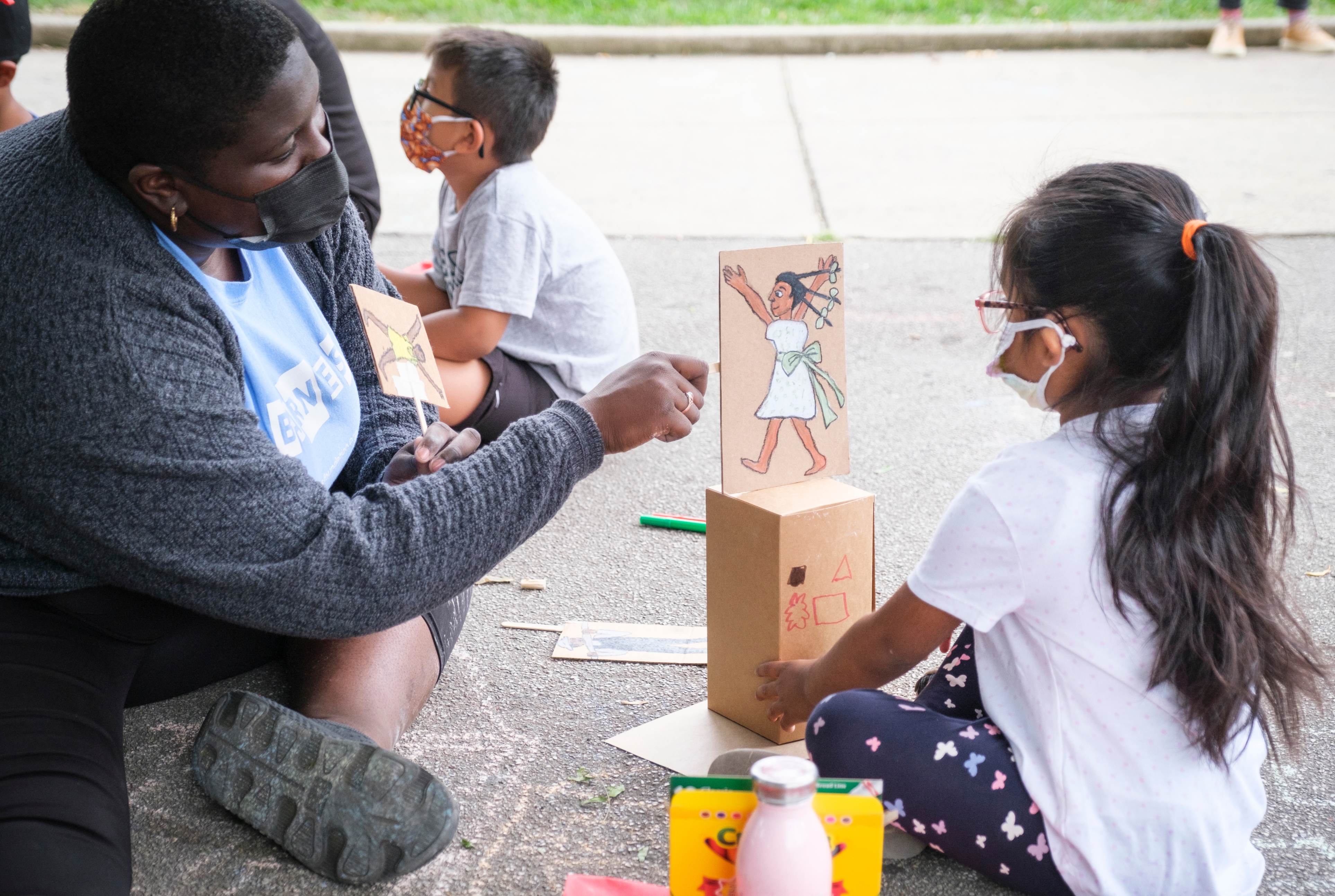 A woman and a young girl sitting on the ground looking at a drawing