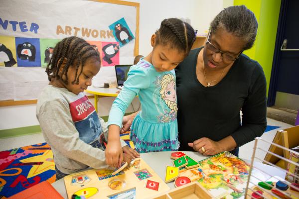 Teacher works with two elementary school children playing with puzzles.