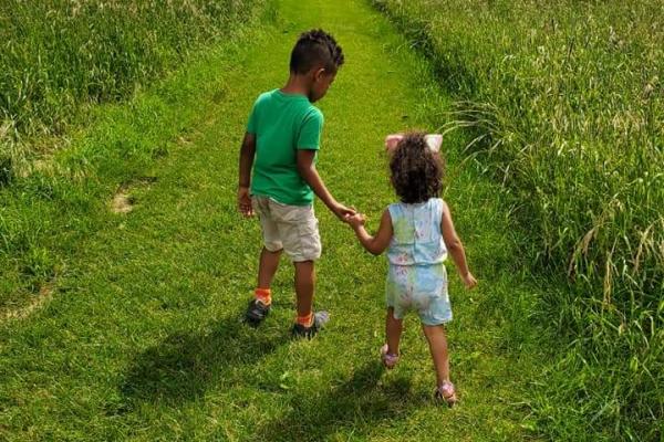 Two children, holding hands, walking down a grass path