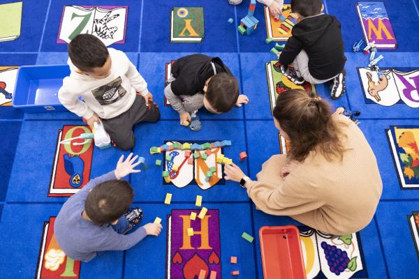An overhead view of a teacher and young children playing with blocks.